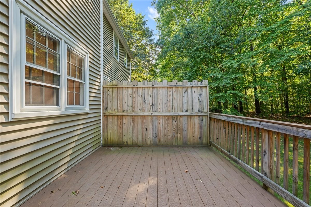 Wooden deck with a tall privacy fence and railing overlooking leafy trees.