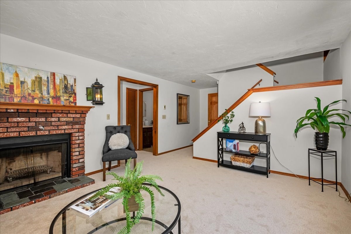 Living room with a brick fireplace, glass coffee table, and staircase with wood trim.