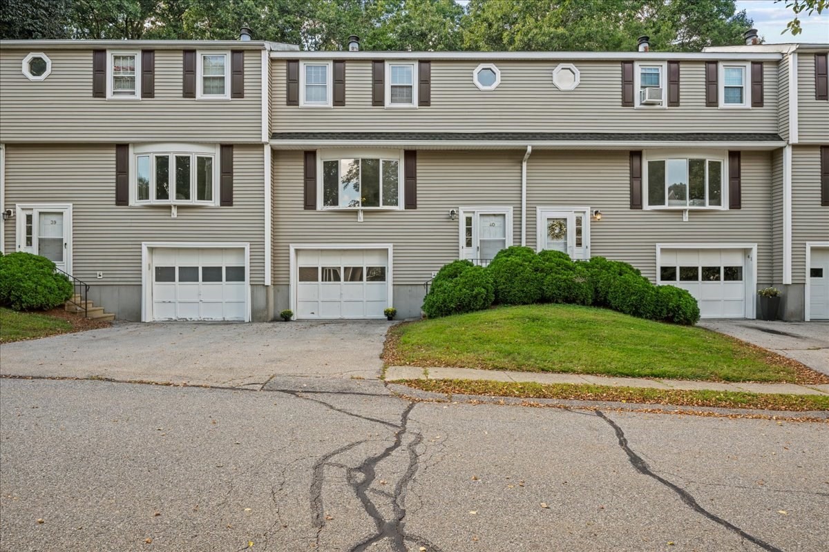 Attached gray townhouses with brown shutters, garage doors, and shrubs along the front.