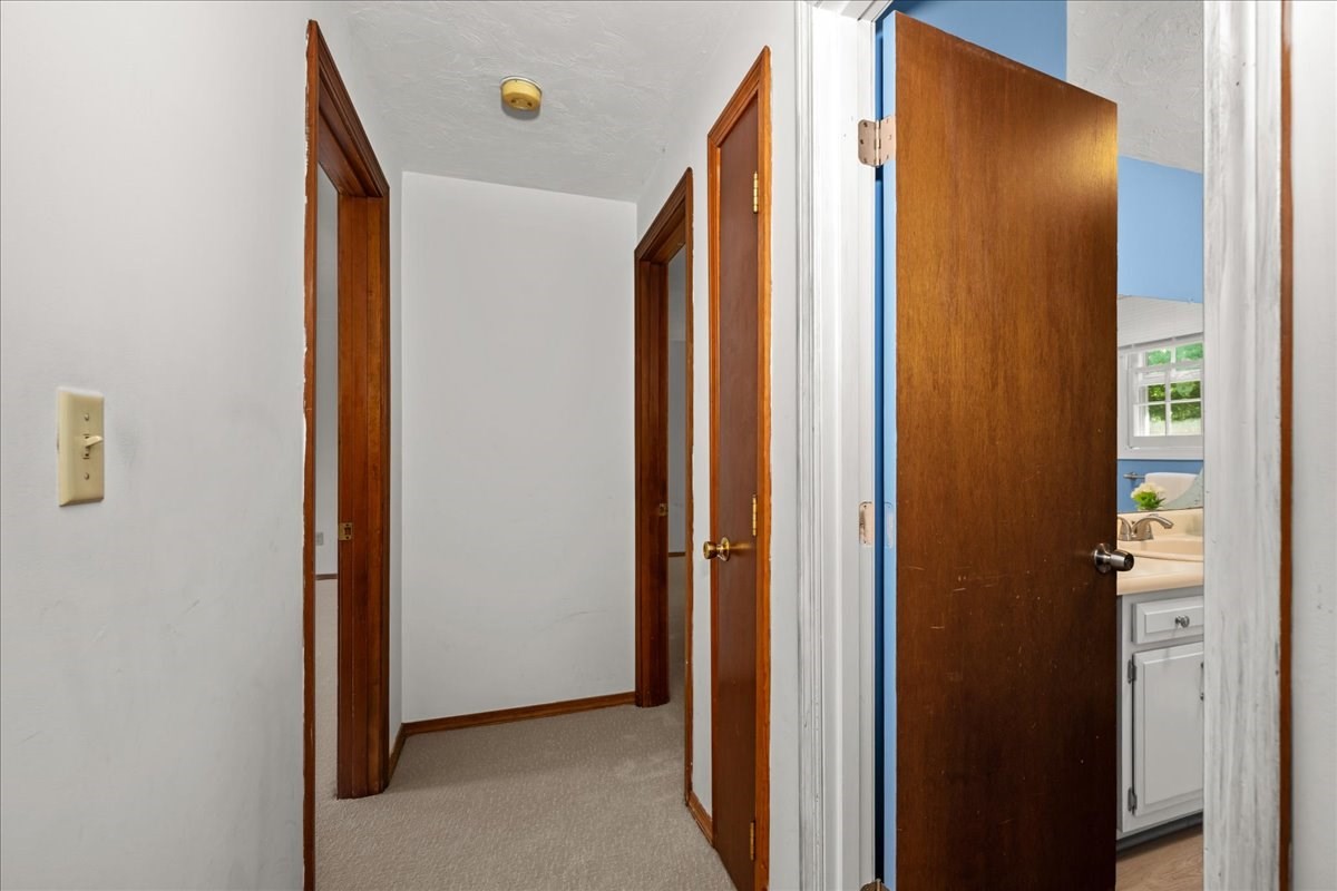Carpeted hallway with dark wood trim and open doors revealing a blue bathroom.