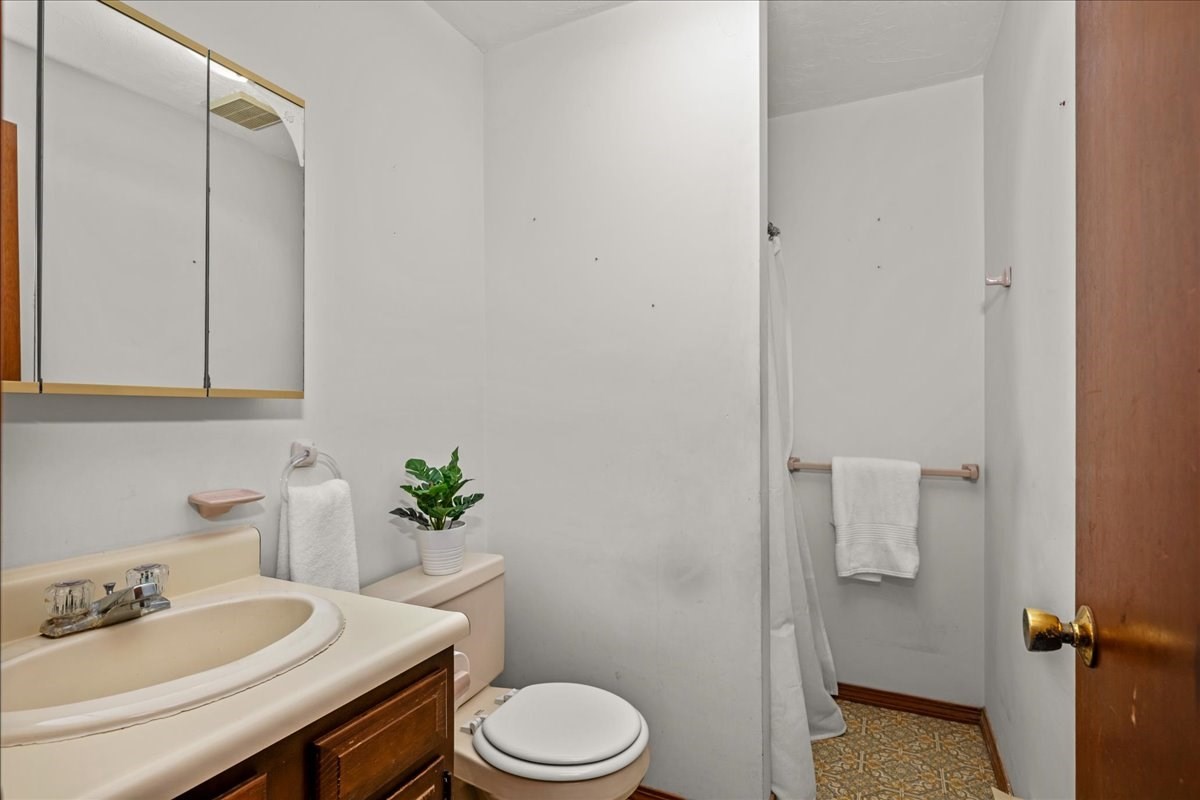 Bathroom with a beige sink and wood vanity, mirrored cabinet, and curtained shower.