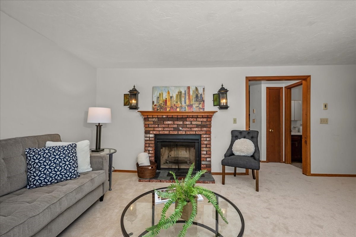 Living room with a brick fireplace, gray sofa, and glass coffee table topped with a fern.