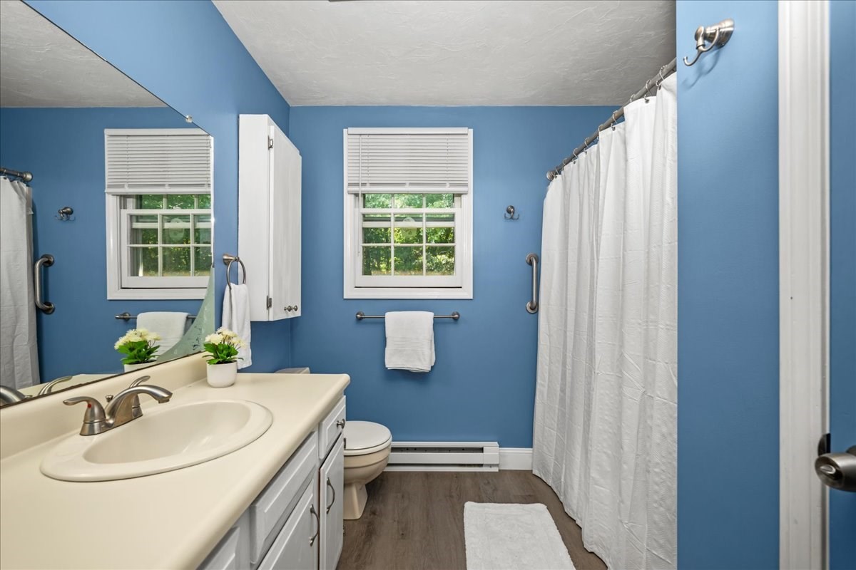 Blue bathroom with white vanity, two windows, and a white shower curtain.