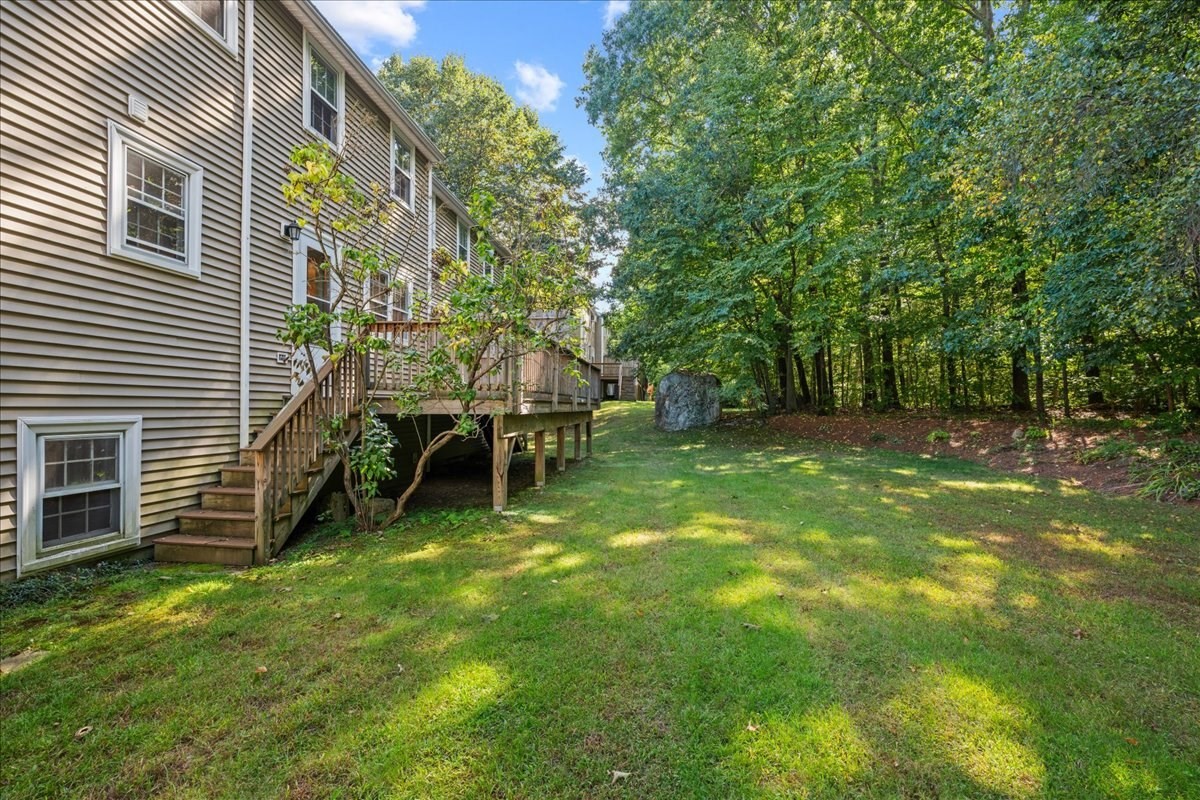 Home’s rear exterior with a raised deck, broad lawn, and wooded backyard.