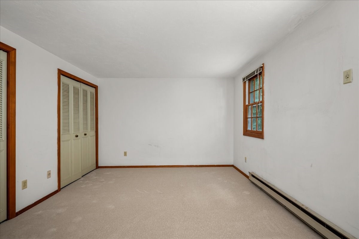 Empty carpeted bedroom with a louvered closet and wood-trimmed window.
