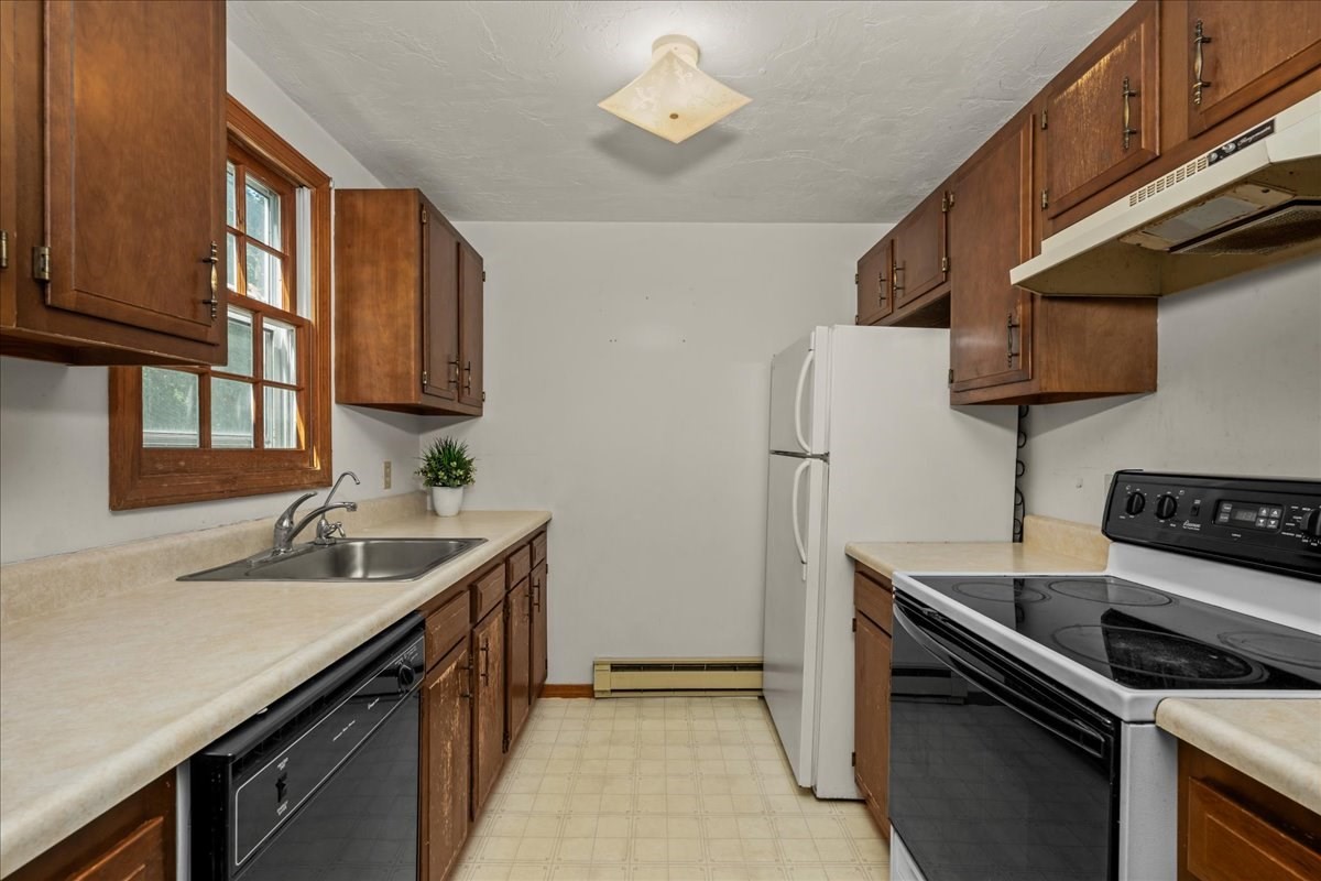 Kitchen with dark wood cabinets, a sink beneath the window, and a white refrigerator.