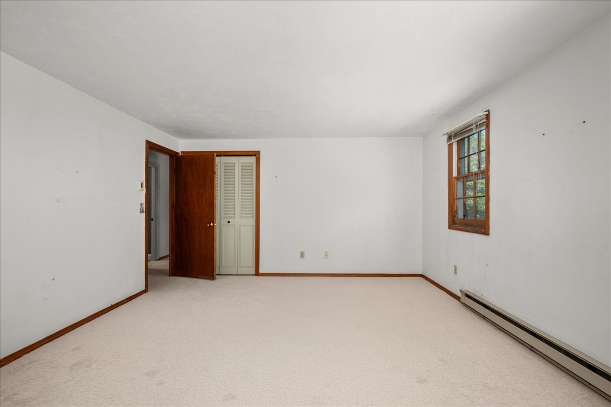Empty bedroom with light carpet, a wood-trimmed window, and an open closet.