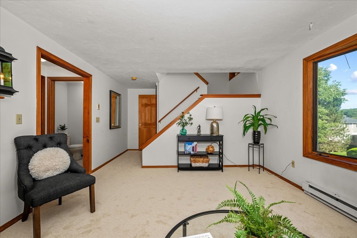 Living room with a wood-trimmed staircase, dark chair, and large window overlooking trees.