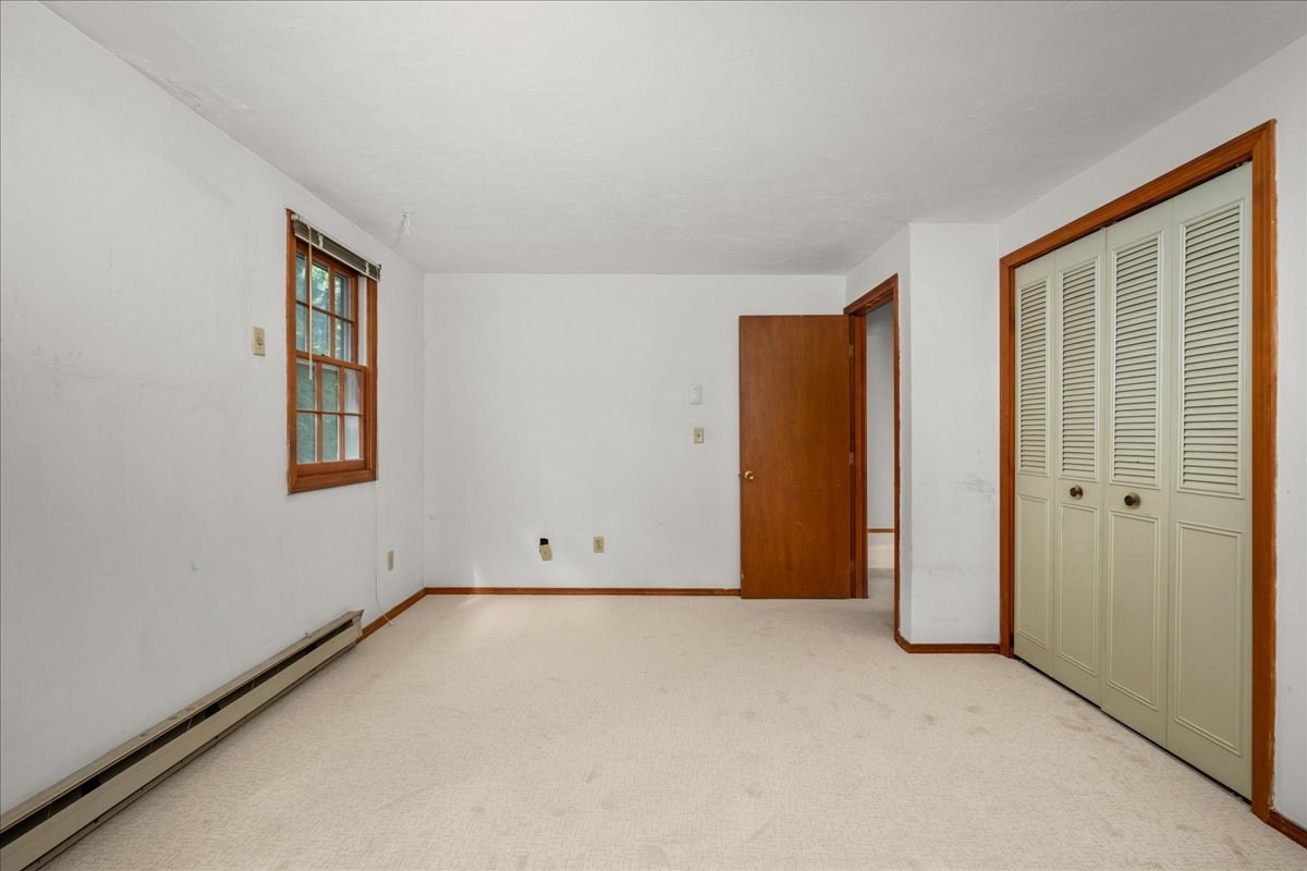 Empty bedroom with light carpet, wood-trimmed window, and louvered closet doors.