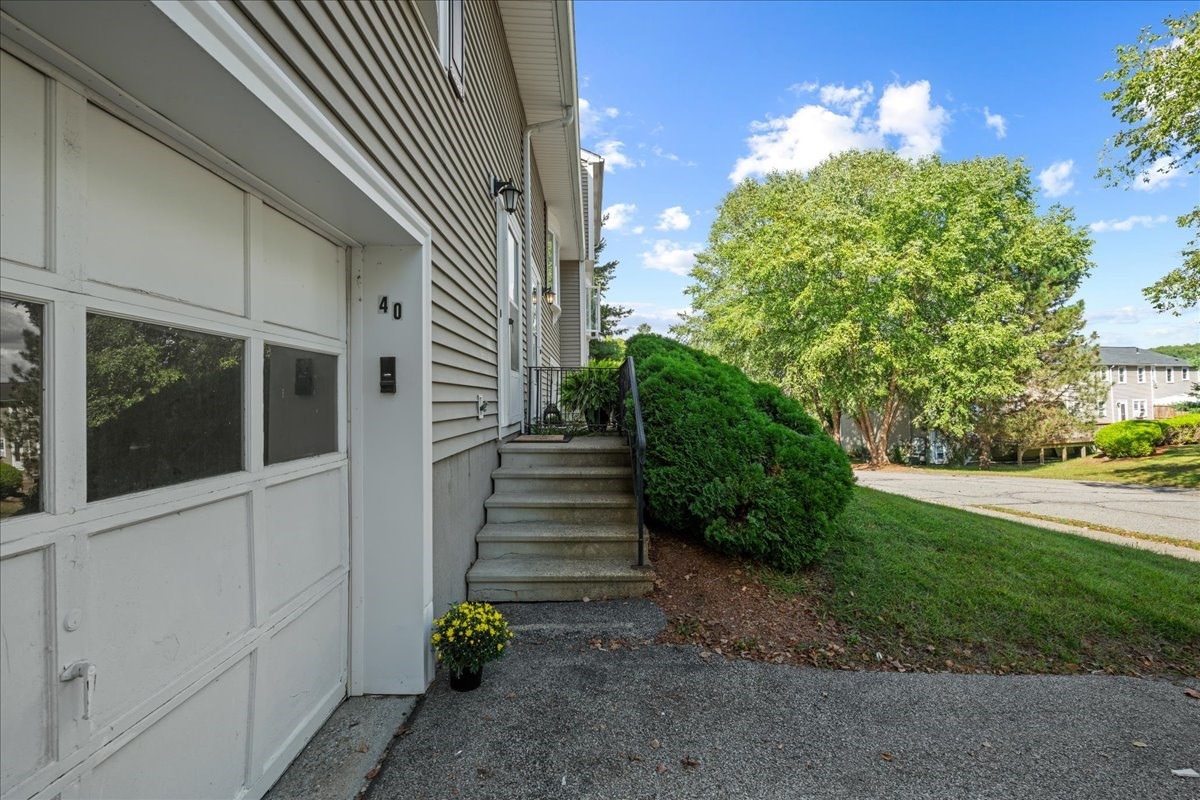 Unit 40 entrance beside a white garage door, concrete steps, and shrubs.
