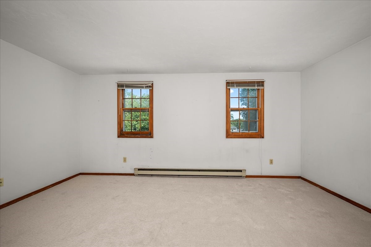 Vacant carpeted room with two wood-trimmed windows and a baseboard heater.