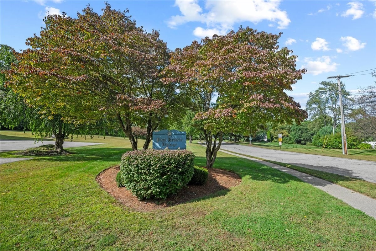 Residential community entrance sign among trimmed shrubs and mature trees beside a paved road.