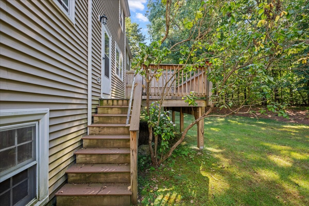 Home exterior with wooden stairs to a raised deck beside a leafy backyard.