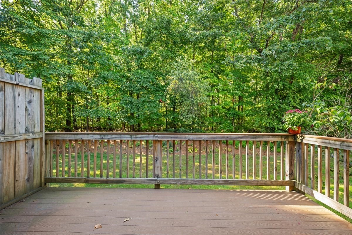 Wooden deck overlooking a leafy backyard, with a potted flowering plant on the railing.