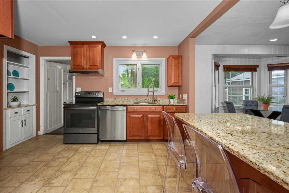 Kitchen with reddish wood cabinets, granite counters, stainless steel appliances, and a large peninsula.