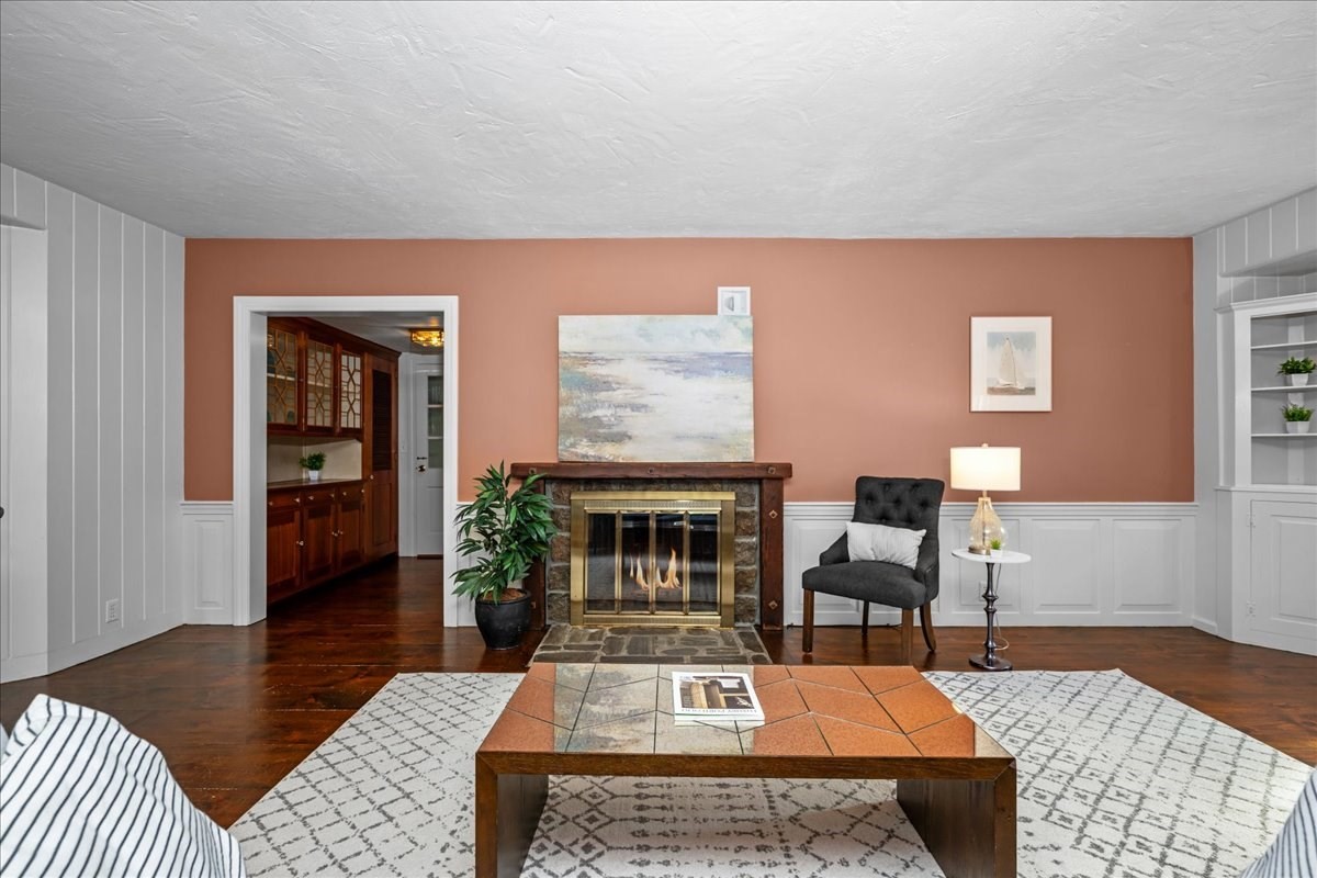 Living room with a stone fireplace, terracotta walls, dark wood floors, and built-in cabinetry beyond the doorway.