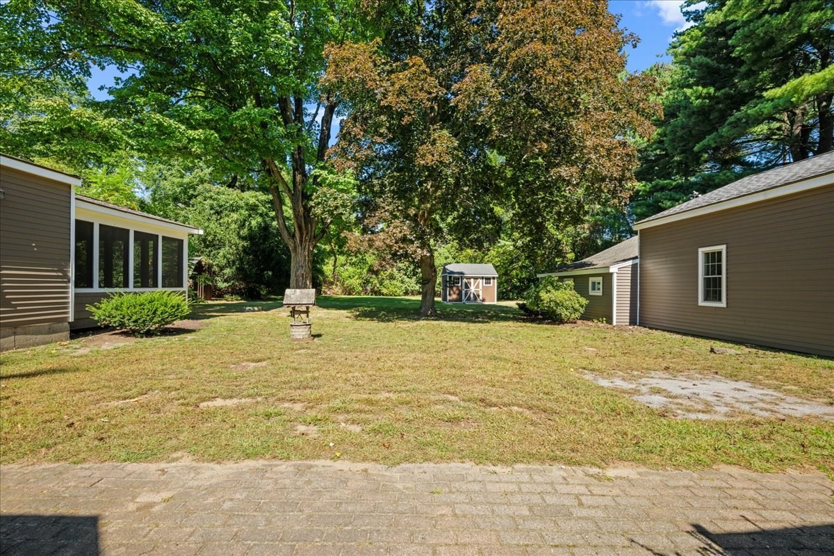 Backyard with a broad lawn, mature trees, and a small shed between house wings.
