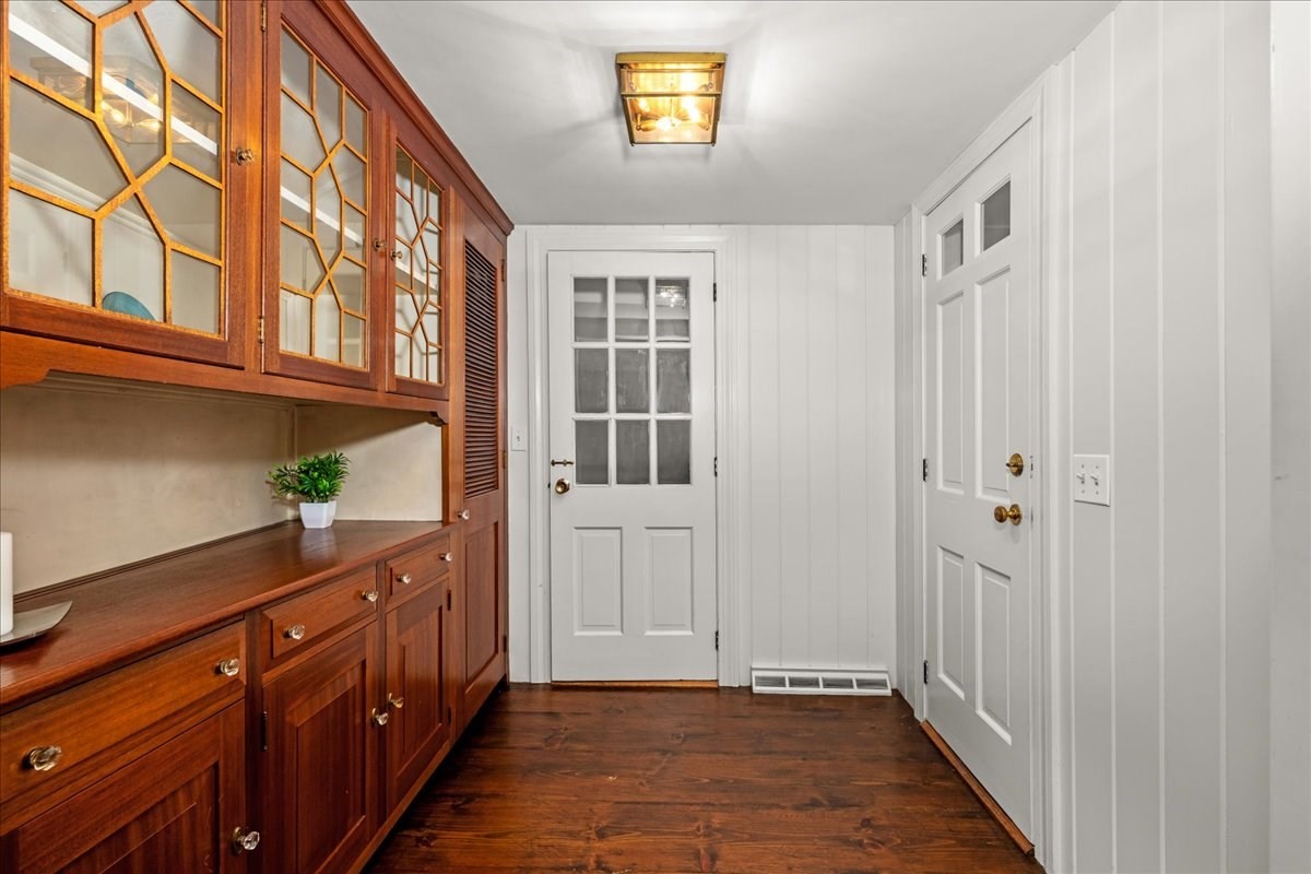 Entryway with glass-front wood cabinetry, dark hardwood floors, and white paneled walls.