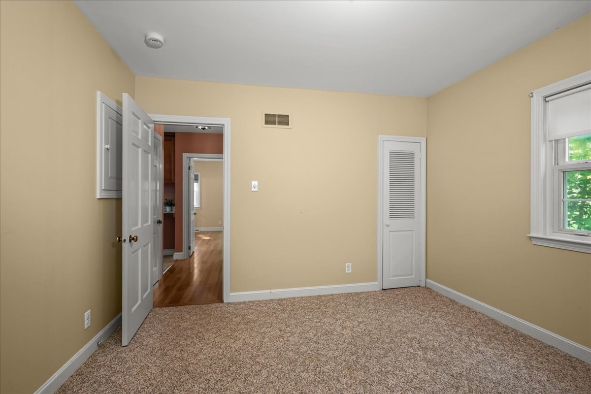 Empty bedroom with tan carpet, beige walls, and a louvered closet door.