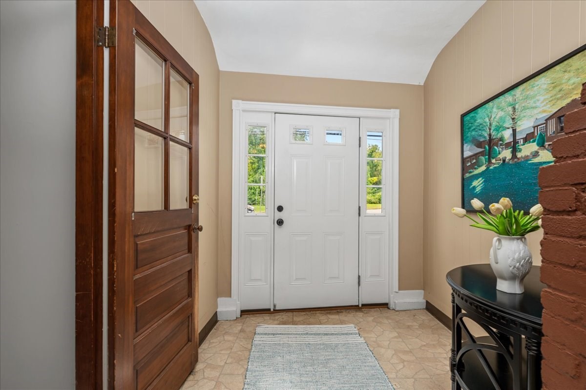 Entry foyer with a white front door, patterned tile floor, and console table with flowers.