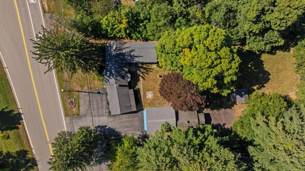 Aerial view of buildings and paved areas beside a road, surrounded by mature trees.