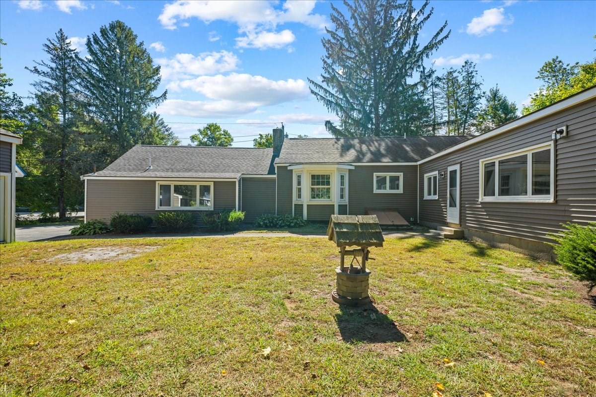 Rear of a gray single-story home across a grassy yard, with a small wishing well in front.