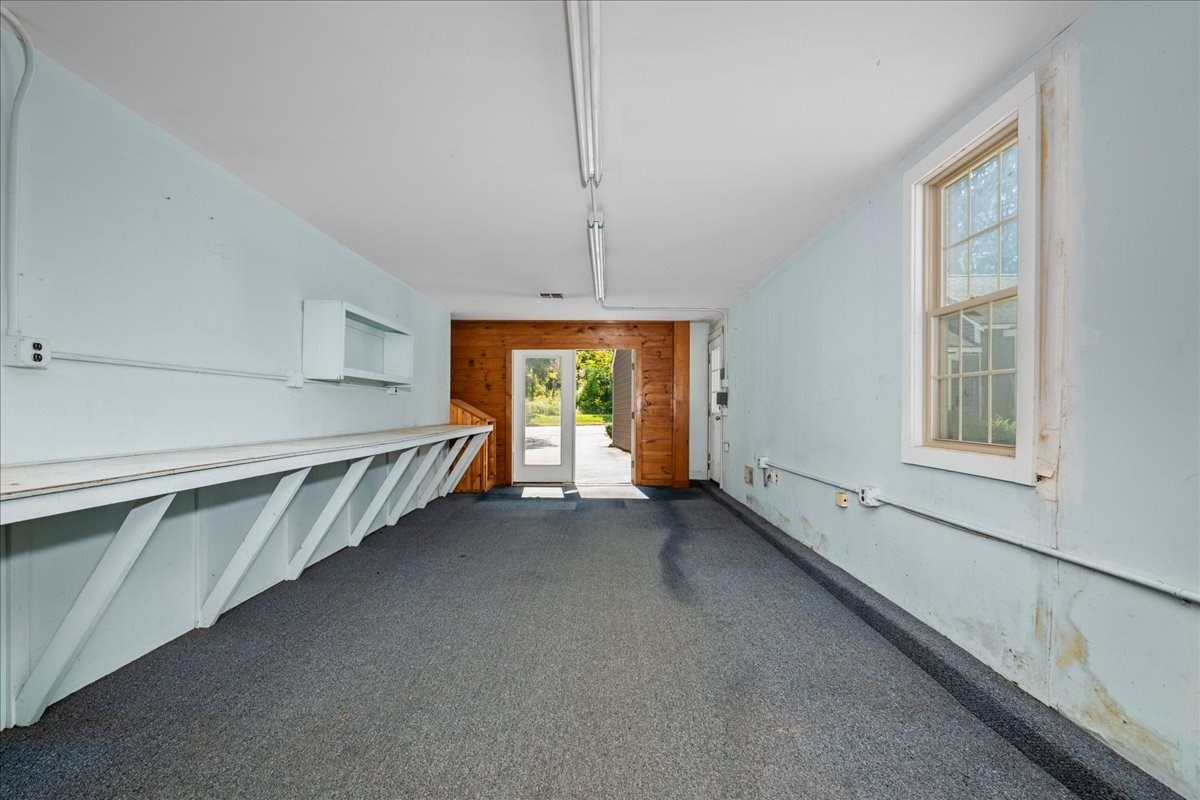 Empty garage with a long built-in workbench and an open door to the outdoors.