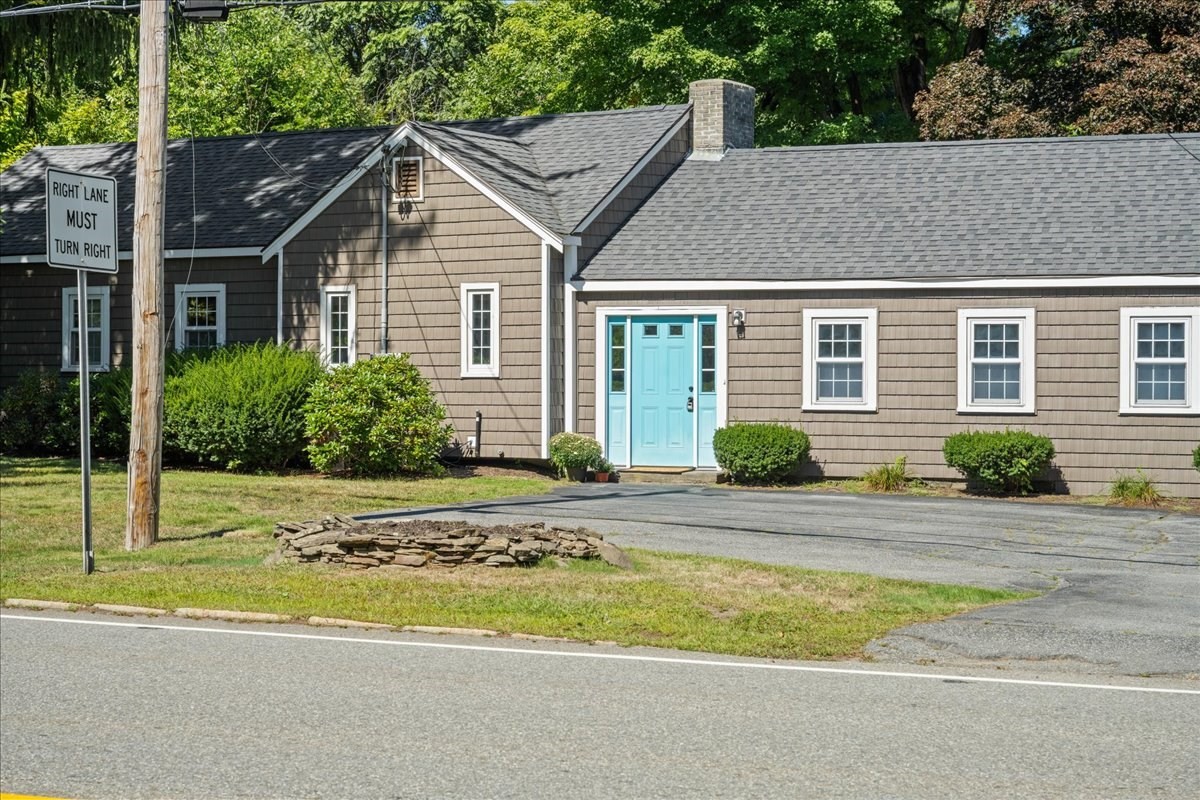 Taupe shingle-sided house with a bright turquoise front door and paved parking area.