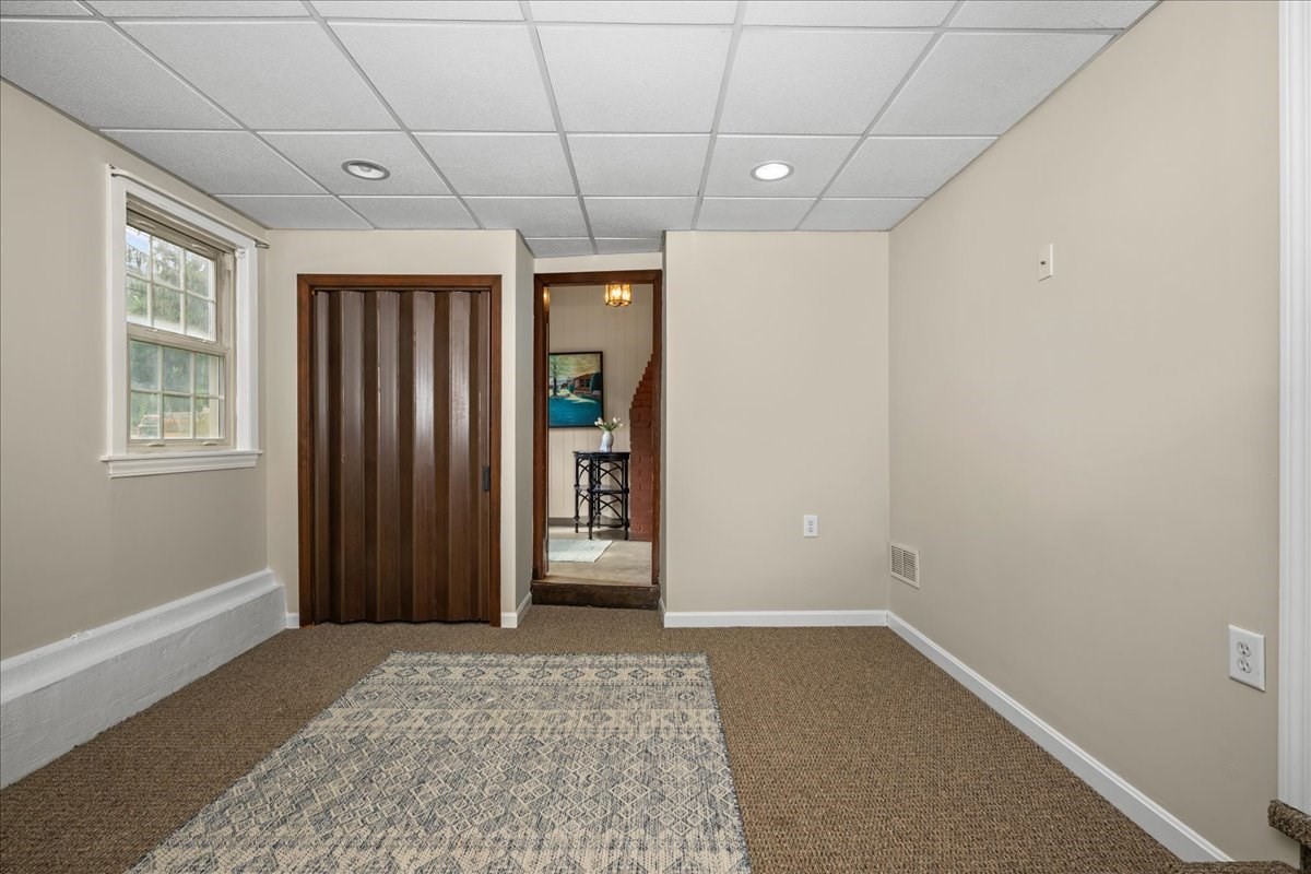 Carpeted room with a patterned rug, window, dark wood folding door, and doorway to a staircase.