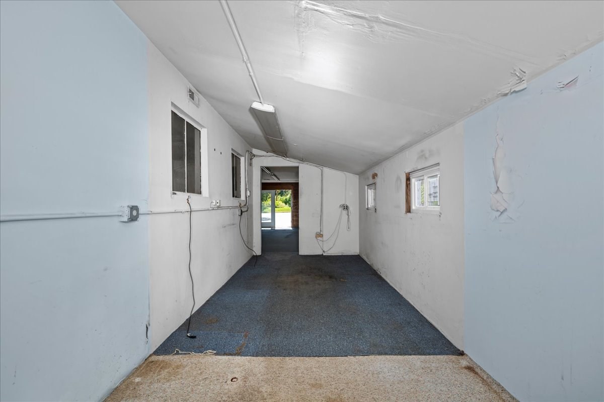 Empty narrow room with blue carpet, small windows, and peeling paint.