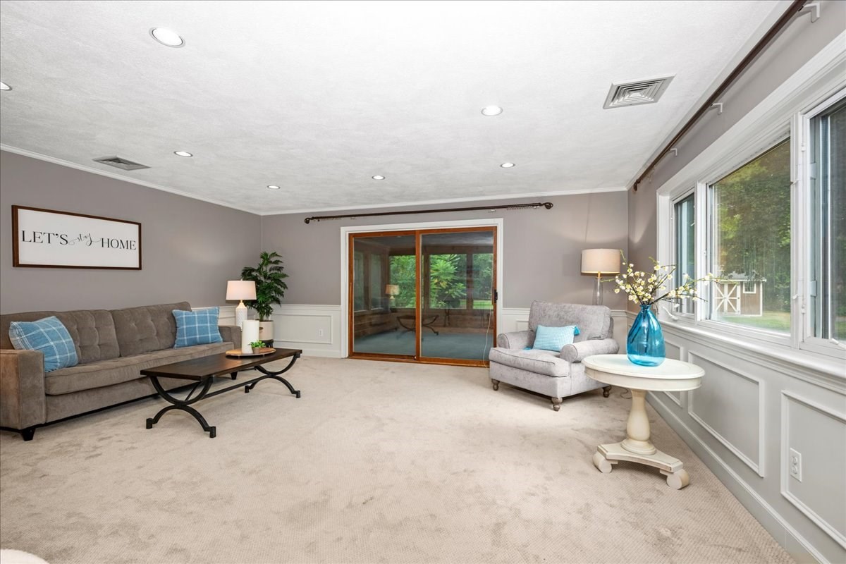Staged living room with a gray sofa, large windows, and sliding glass doors overlooking greenery.
