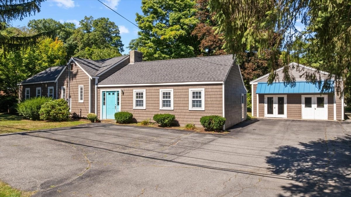 Brown shingle-sided building with a turquoise door beside a matching outbuilding with a blue awning.