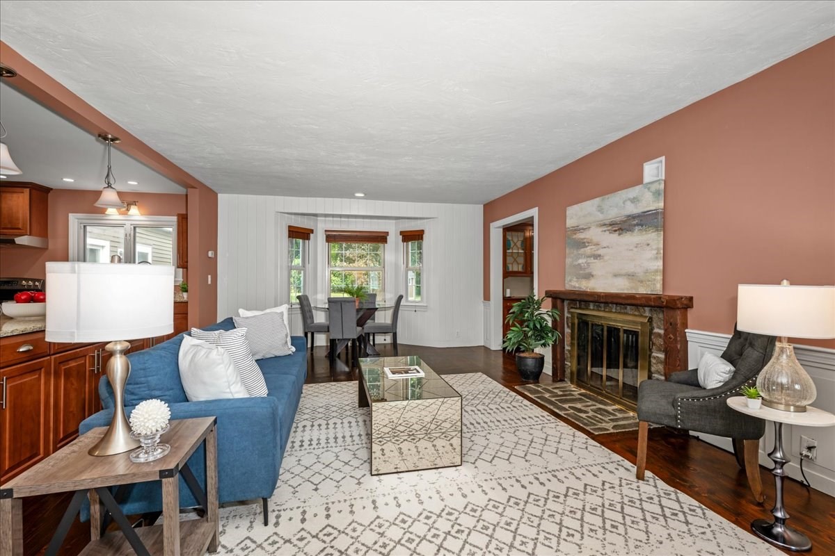 Staged living room with blue sofa, patterned rug, and wood-trimmed fireplace beside the dining area.
