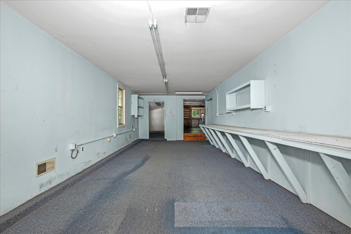 Vacant long room with pale blue walls, gray carpet, and a built-in workbench.