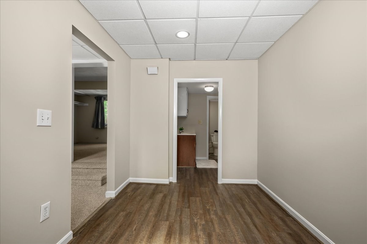 Empty room with wood-look flooring and doorways to a carpeted area and bathroom.