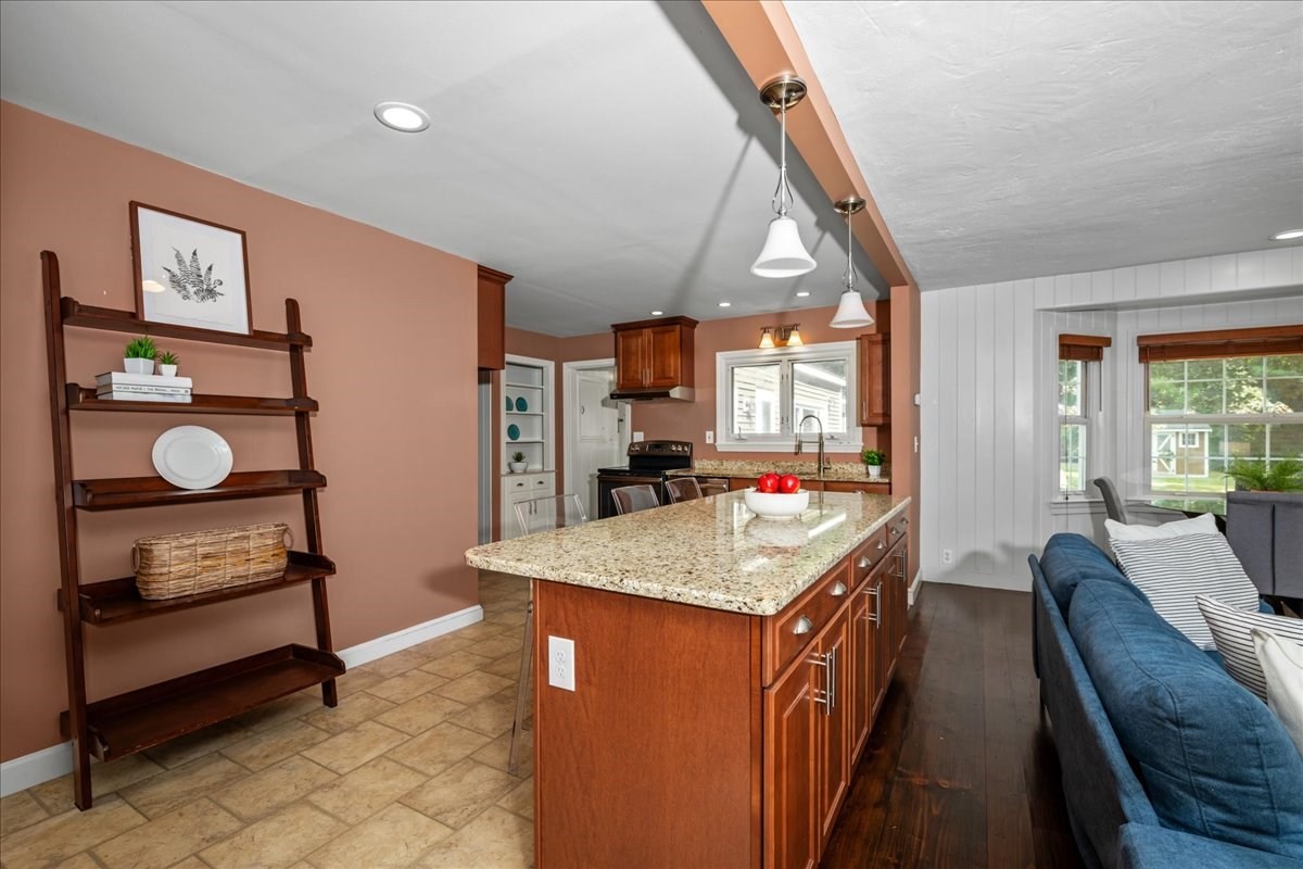 Open-plan kitchen with a granite island and wood cabinets beside a living area with a blue sofa.