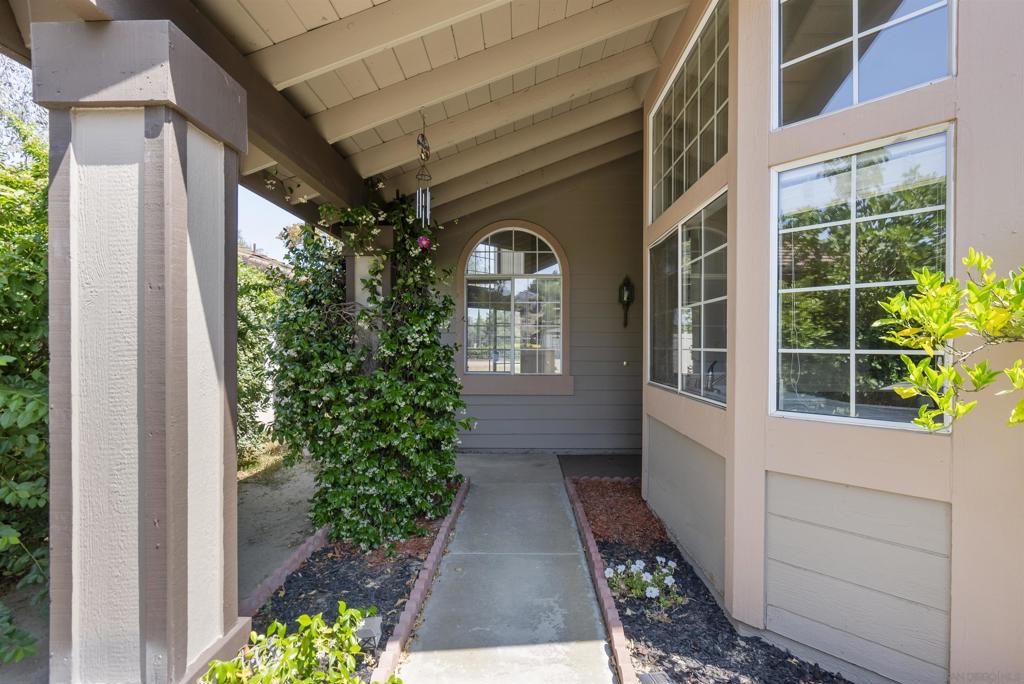Covered front entry walkway with flowering vines, an arched window, and tall exterior windows.