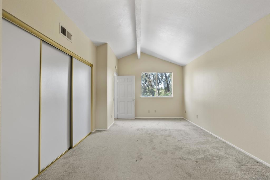 Empty bedroom with sliding closet doors, vaulted ceiling, and a window overlooking trees.