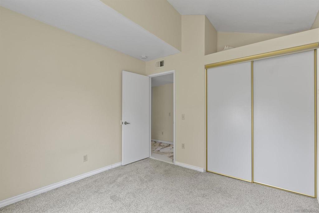 Empty bedroom with light carpet and gold-trimmed sliding closet doors.