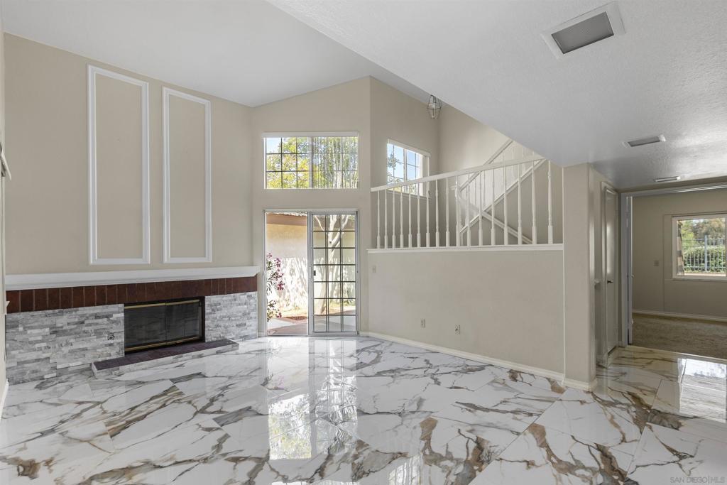 Unfurnished living room with marble-look tile, a fireplace, vaulted ceiling, and staircase.