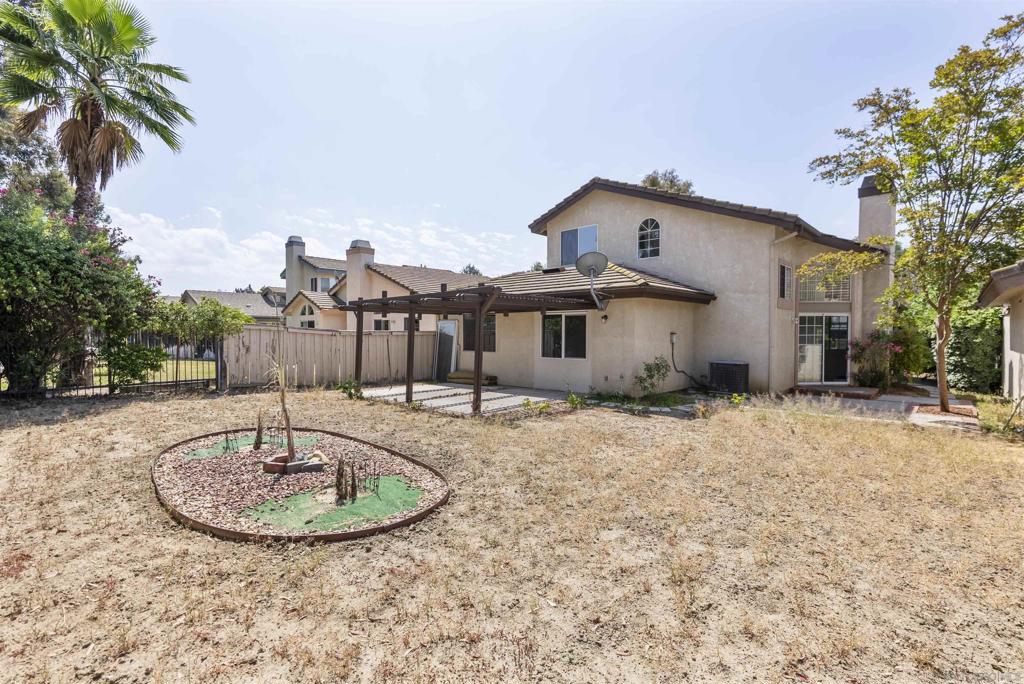 Rear of a two-story stucco home with a pergola patio and dry backyard.