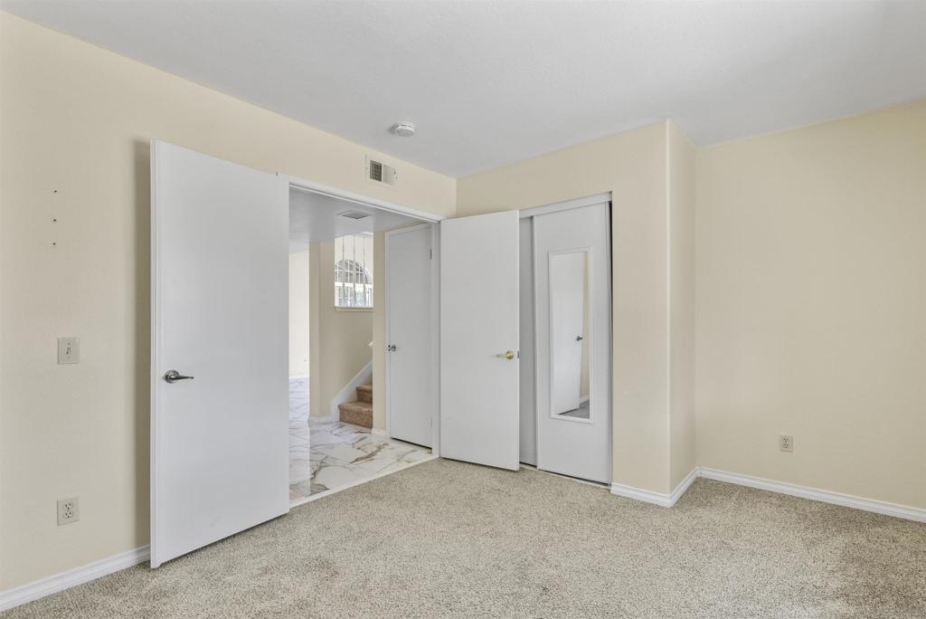 Empty carpeted bedroom with open doors and a mirrored closet door.