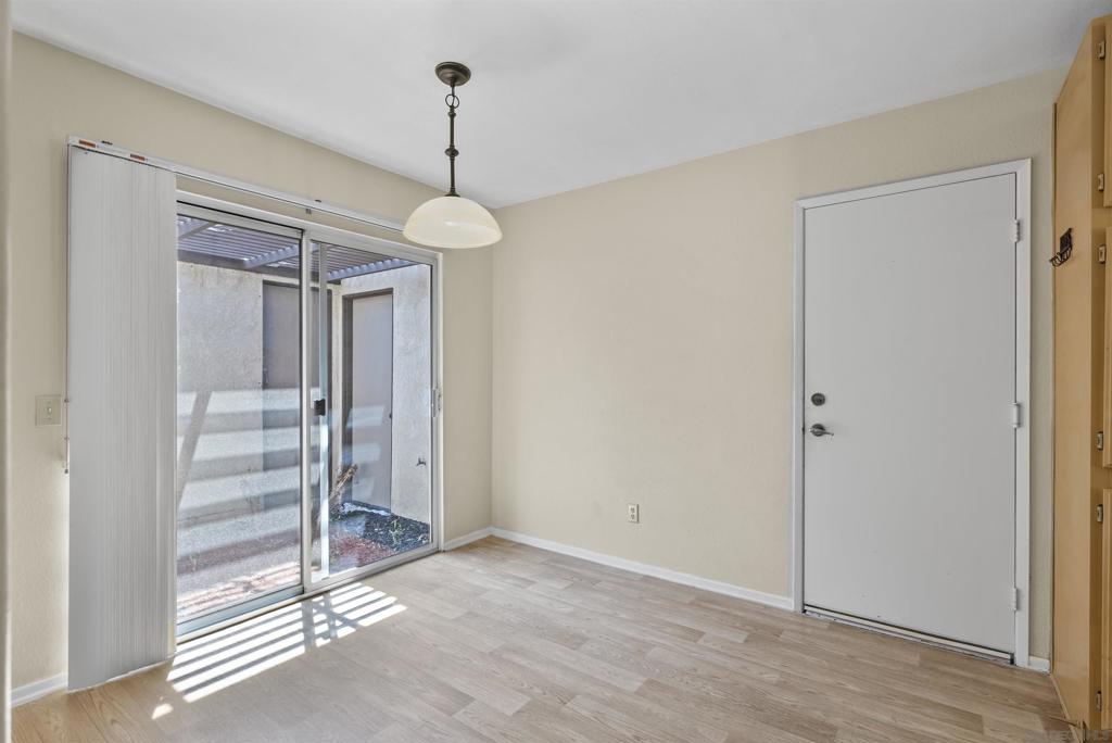 Empty room with light wood-look floors, a pendant light, and sliding glass doors to an enclosed outdoor area.