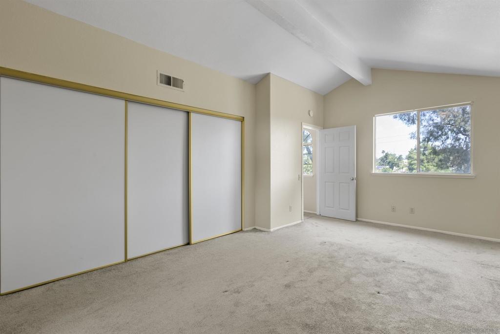 Empty carpeted bedroom with gold-trimmed sliding closet doors and a large window.