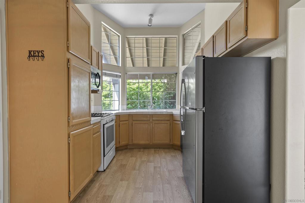 Kitchen with honey-colored cabinets, a black refrigerator, and large windows overlooking greenery.