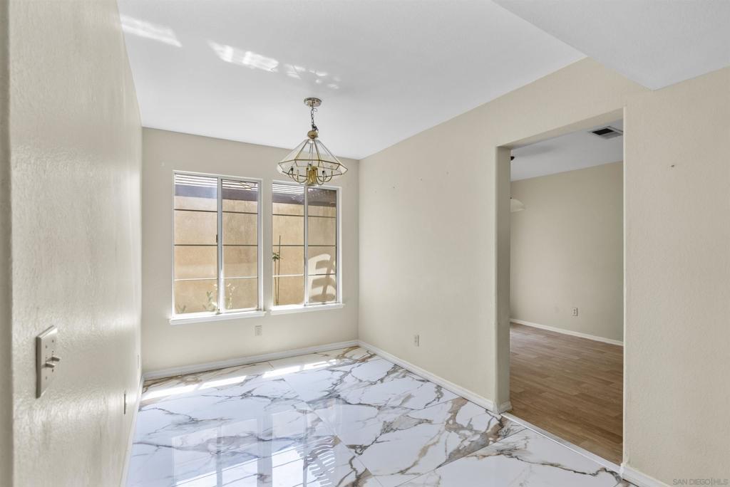 Vacant room with a chandelier, large windows, and glossy marble-look tile flooring.
