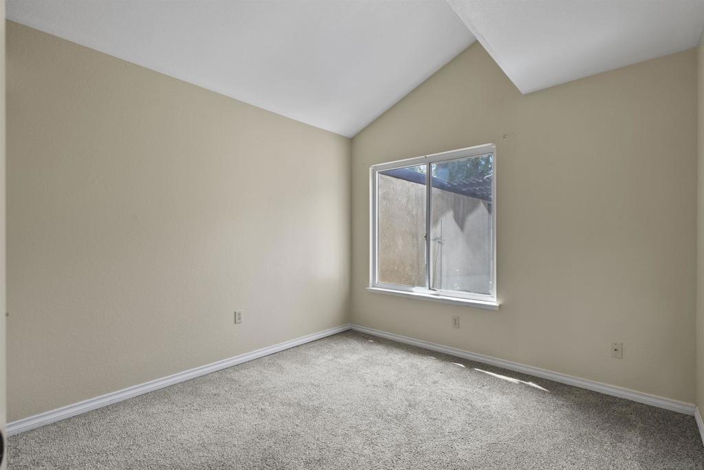 Empty bedroom with gray carpet, a large window, and a vaulted ceiling.