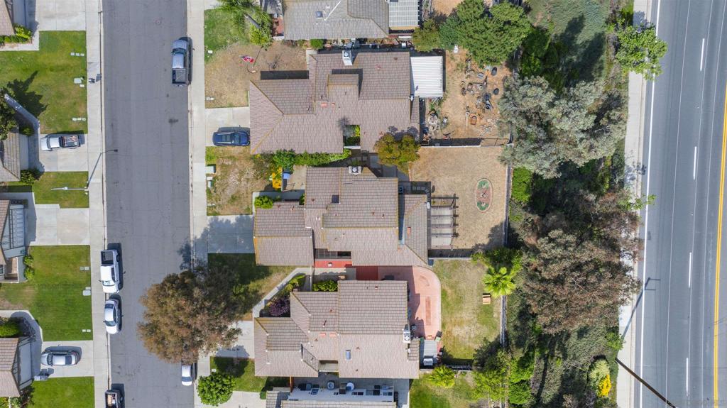 Aerial view of a tiled-roof home with a fenced backyard and patio beside a residential street.