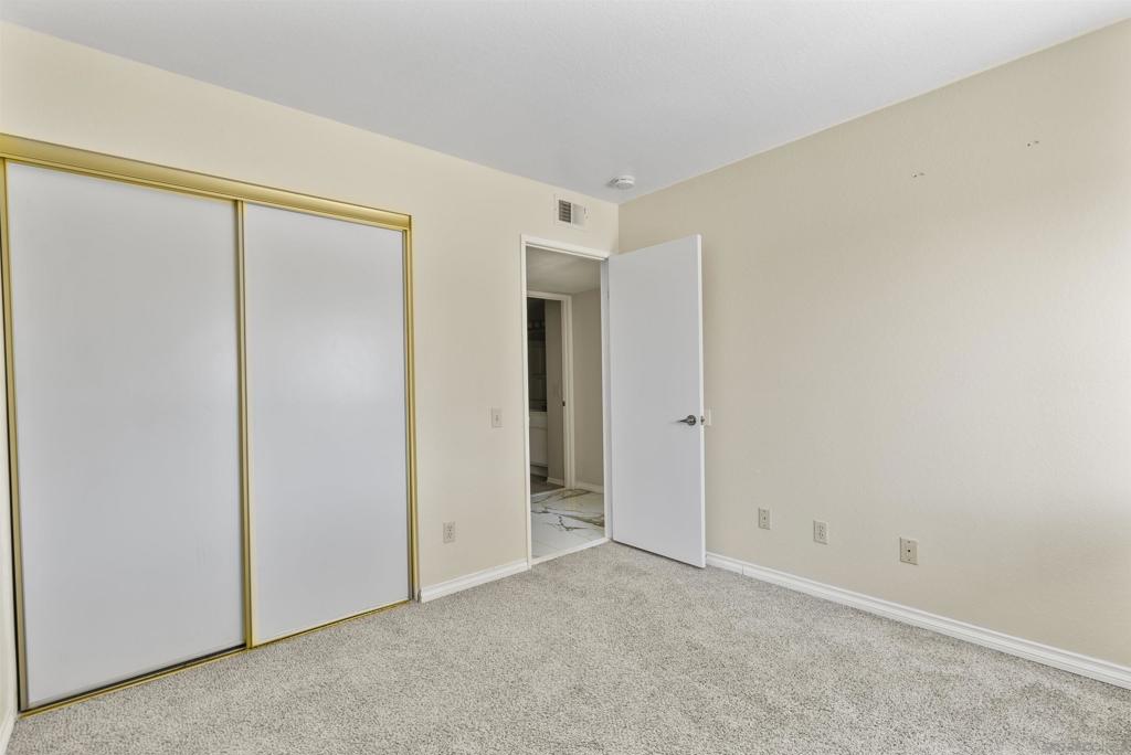 Empty bedroom with a gold-trimmed sliding closet and an open door to a tiled area.