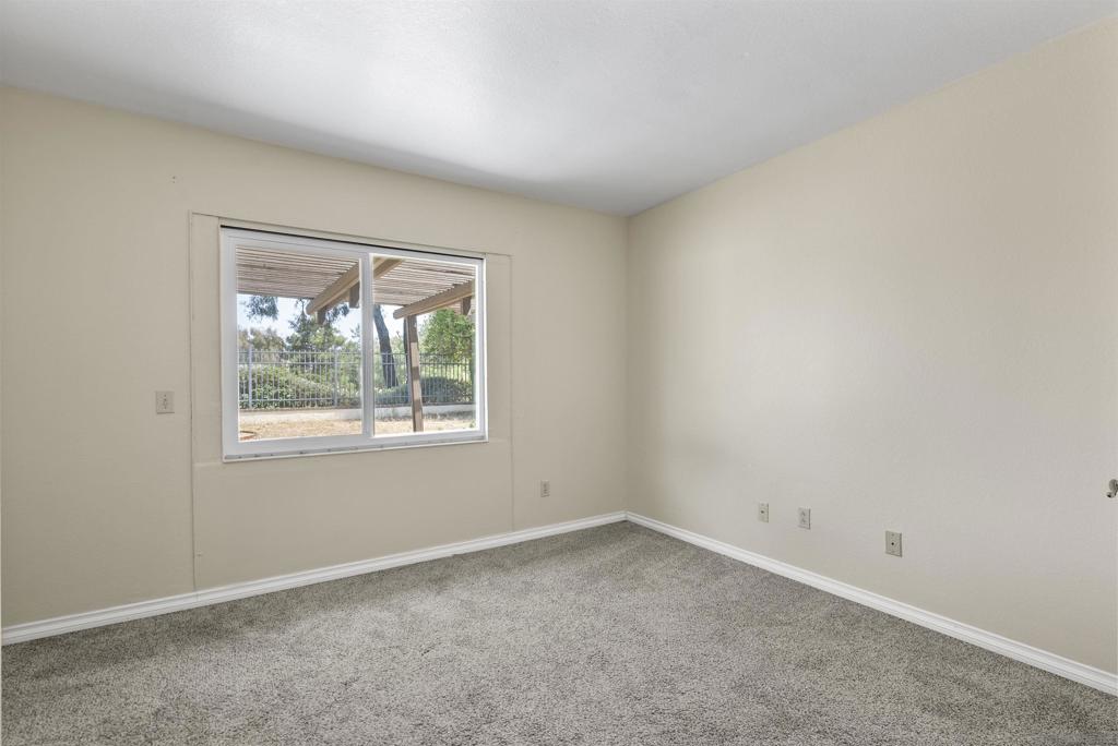 Empty bedroom with gray carpet and a window overlooking a fenced yard and covered patio.